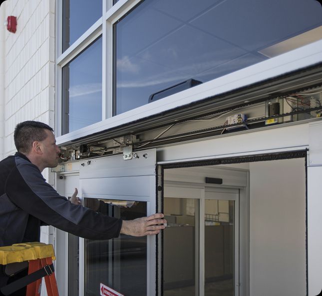 Technician performing commercial door services in Buffalo, NY, repairing the track and operator system of an automatic sliding door.