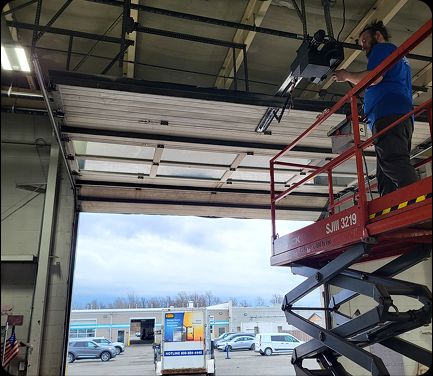 Technician providing commercial door services in Buffalo, NY, repairing an overhead industrial door inside a facility.