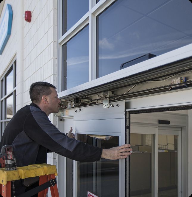 Technician performing commercial door services in Cincinnati, OH, repairing the track and operator system of an automatic sliding door.